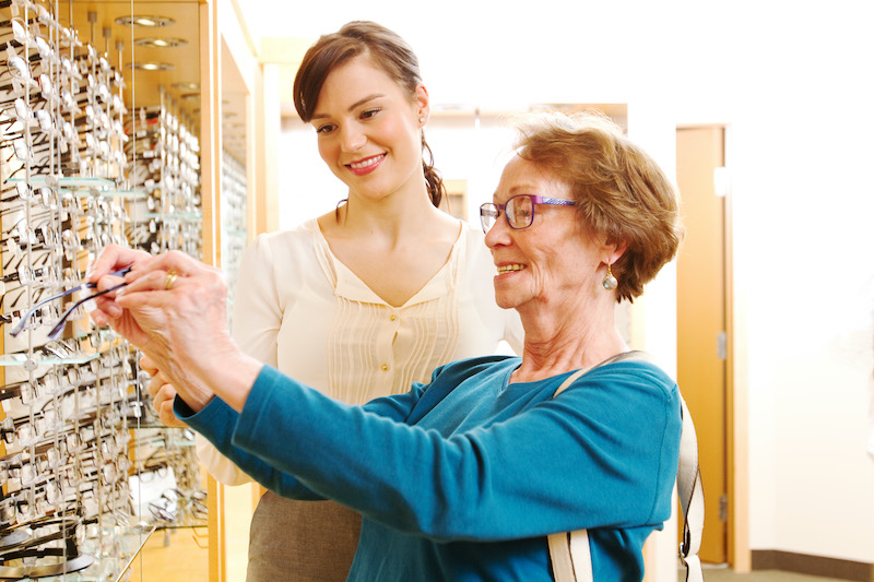 Optician assisting older lady with glasses Optikerin und Kundin im Geschäft
